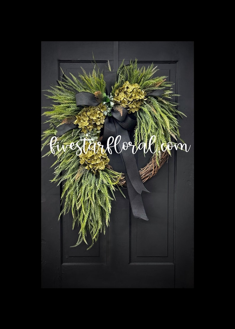May include: A green and black wreath with a black ribbon bow. The wreath is made of greenery and has a cluster of green hydrangeas. The wreath is hanging on a black door. The text "fivestarfloral.com" is visible in the image.