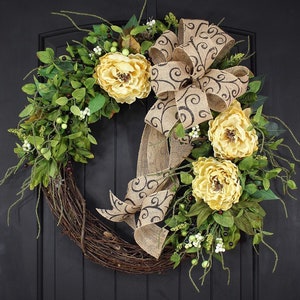 Pode incluir: Uma coroa de videira com um la&ccedil;o de juta e flores amarelas. O la&ccedil;o tem um padr&atilde;o de espiral preto.