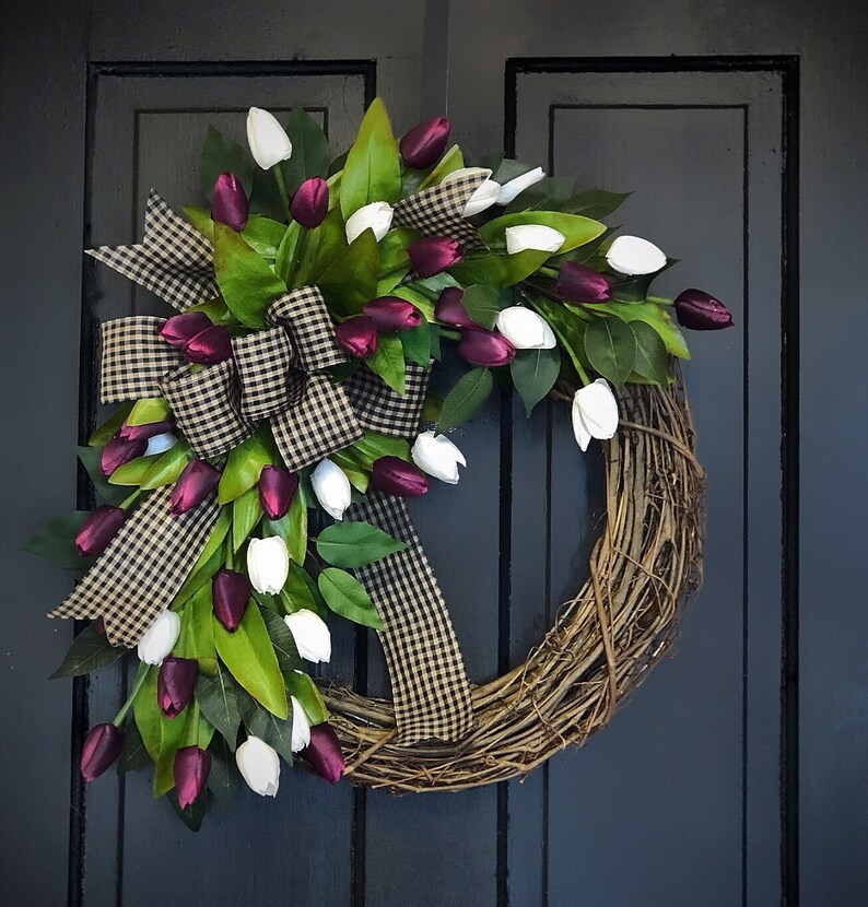 May include: A grapevine wreath decorated with white and burgundy artificial tulips and a black and white checkered ribbon.