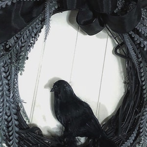 May include: A black wreath with a black crow perched on it. The wreath is made of twigs and has black ribbon and black leaves.