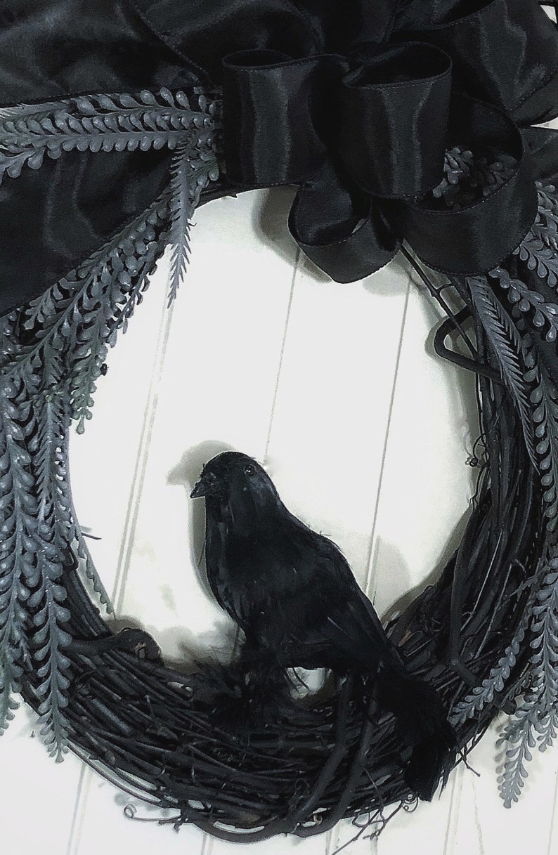 May include: A black wreath with a black crow perched on it. The wreath is made of twigs and has black ribbon and black leaves.
