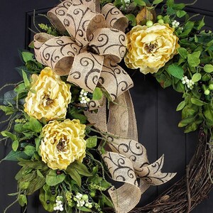 Pode incluir: Uma coroa de juta marrom com um grande la&ccedil;o e flores amarelas. O la&ccedil;o tem um padr&atilde;o de espiral marrom. A coroa &eacute; decorada com folhas verdes e bagas brancas.
