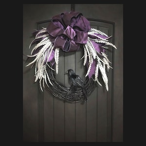 Puede incluir: Un cuervo negro posado en una corona de ramas con un lazo de sat&eacute;n morado y detalles de plumas blancas. La corona est&aacute; colgada en una puerta de madera oscura.