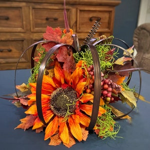 Peut inclure: Une pi&egrave;ce ma&icirc;tresse sur le th&egrave;me de l'automne avec un faux tournesol entour&eacute; de cerceaux en m&eacute;tal brun, de feuilles d'automne et de mousse verte.
