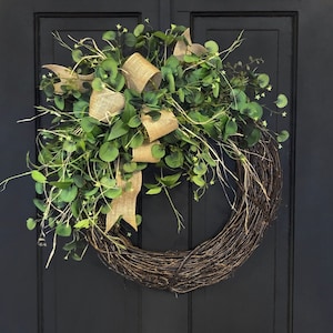 May include: A brown twig wreath with a burlap bow and green eucalyptus leaves. The wreath is hanging on a black door.