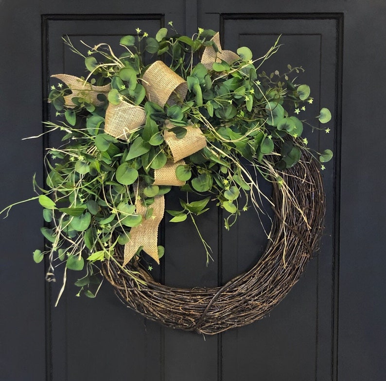 May include: A brown twig wreath with a burlap bow and green eucalyptus leaves. The wreath is hanging on a black door.