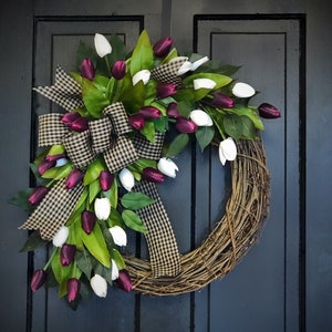 May include: A grapevine wreath decorated with white and burgundy artificial tulips and a black and white checkered bow.
