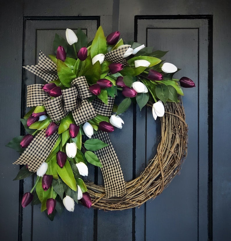 May include: A grapevine wreath decorated with white and burgundy artificial tulips and a black and white checkered bow.