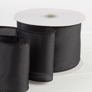Puede incluir: Un rollo de cinta de sat&eacute;n negro con borde alambrado. La cinta tiene 6,35 cm de ancho y una textura suave y sedosa.