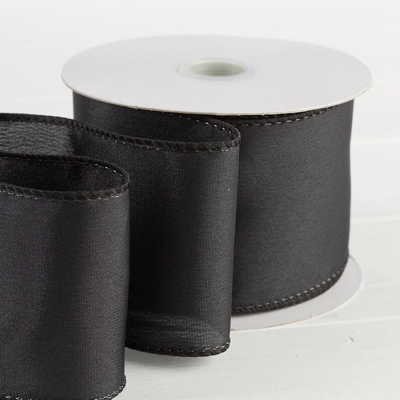 Puede incluir: Un rollo de cinta de sat&eacute;n negro con borde alambrado. La cinta tiene 6,35 cm de ancho y una textura suave y sedosa.