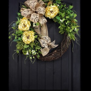 Pode incluir: Uma coroa de ramos marrons com um la&ccedil;o de juta e flores amarelas. O la&ccedil;o tem um padr&atilde;o de espiral marrom. A coroa est&aacute; pendurada em uma porta preta.