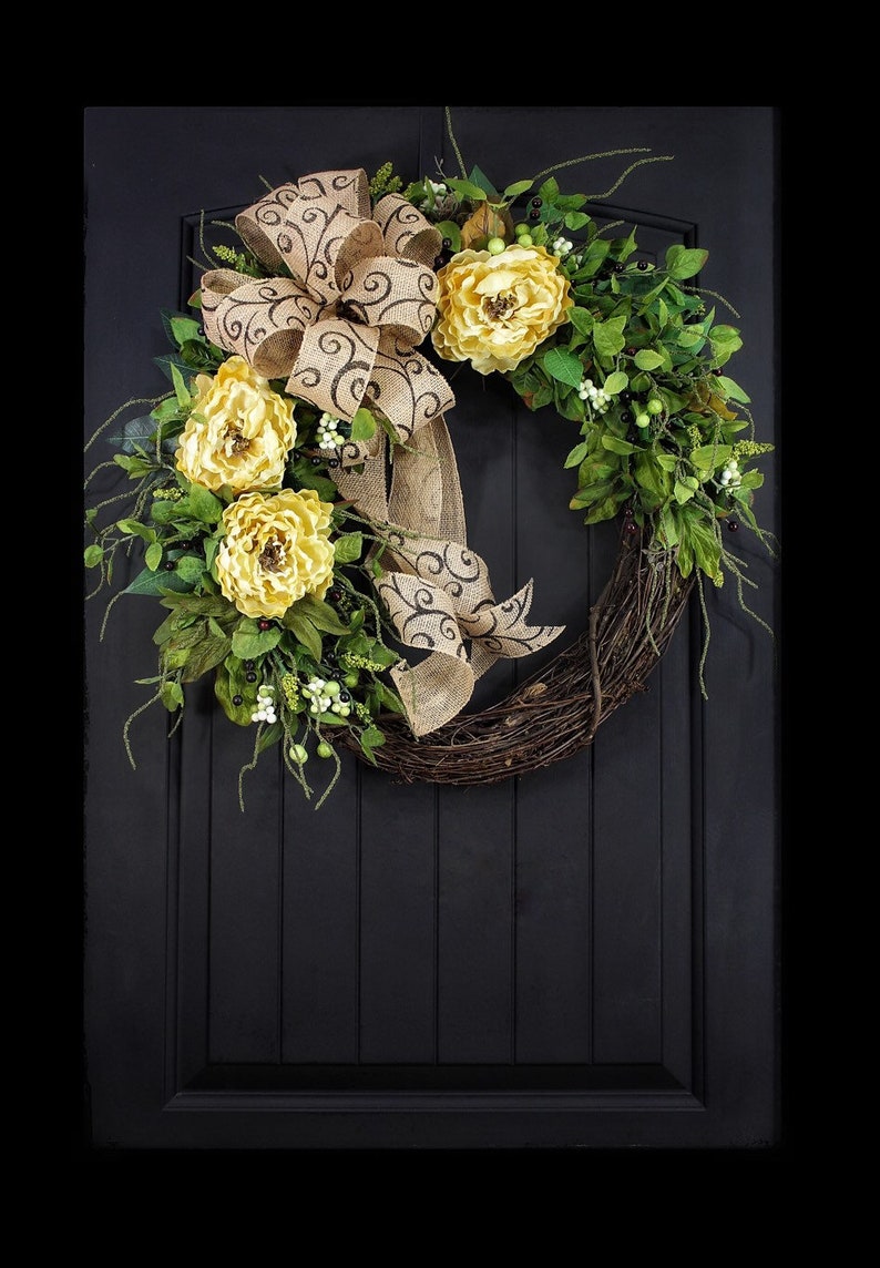 Pode incluir: Uma coroa de ramos marrons com um la&ccedil;o de juta e flores amarelas. O la&ccedil;o tem um padr&atilde;o de espiral marrom. A coroa est&aacute; pendurada em uma porta preta.