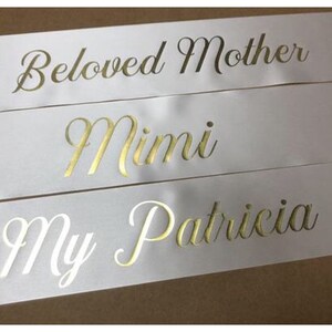 Puede incluir: Tres cintas de sat&eacute;n blanco con letras doradas. La cinta superior dice "Beloved Mother", la cinta del medio dice "Mimi" y la cinta inferior dice "My Patricia".