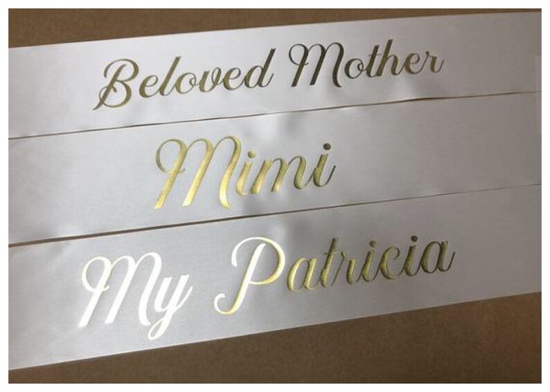 Puede incluir: Tres cintas de sat&eacute;n blanco con letras doradas. La cinta superior dice "Beloved Mother", la cinta del medio dice "Mimi" y la cinta inferior dice "My Patricia".