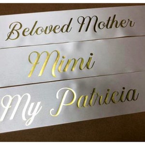 Puede incluir: Tres cintas de sat&eacute;n blanco con letras doradas. Las cintas dicen "Beloved Mother", "Mimi" y "My Patricia".