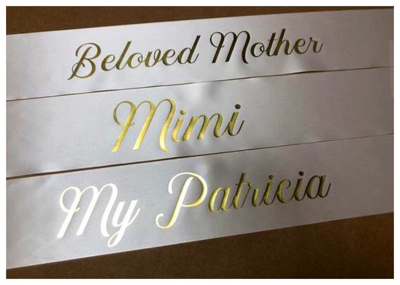 Puede incluir: Tres cintas de sat&eacute;n blanco con letras doradas. Las cintas dicen "Beloved Mother", "Mimi" y "My Patricia".