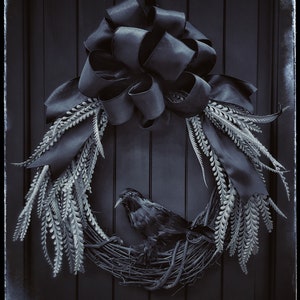 May include: A black crow sits in a wreath made of gray branches and black ribbon. The wreath is decorated with a large black bow.