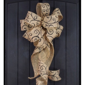 May include: A large burlap bow with a black swirl pattern, hanging on a black door.