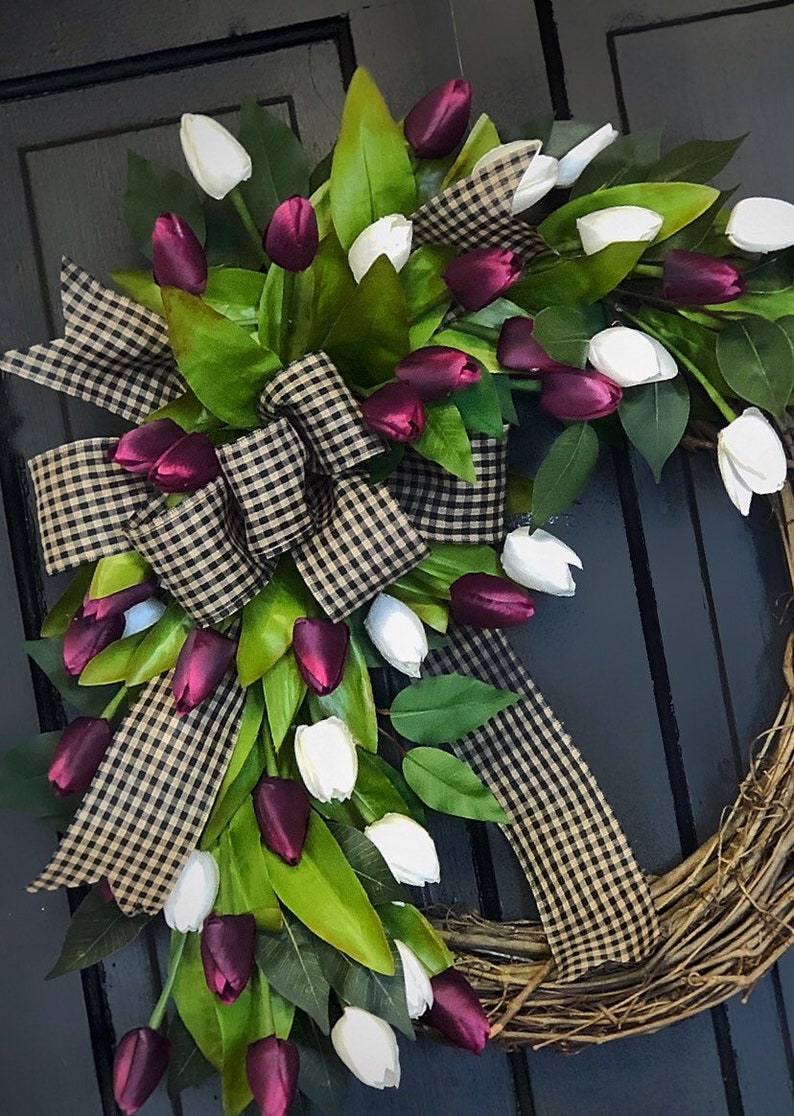 May include: A grapevine wreath decorated with a black and white checkered ribbon and a cascade of burgundy and white tulips.