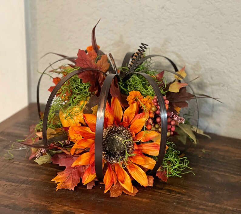 Peut inclure: Une pi&egrave;ce ma&icirc;tresse sur le th&egrave;me de l'automne avec un grand tournesol orange avec des accents de fil de fer brun, entour&eacute; de fausses feuilles, de baies et de mousse.