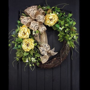 Pode incluir: Uma coroa feita de galhos com um la&ccedil;o de juta e flores amarelas. O la&ccedil;o tem um padr&atilde;o de espiral marrom.