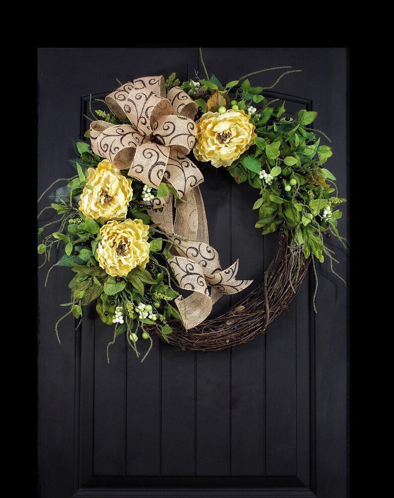 Pode incluir: Uma coroa feita de galhos com um la&ccedil;o de juta e flores amarelas. O la&ccedil;o tem um padr&atilde;o de espiral marrom.