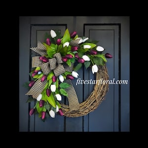 May include: A wreath made of grapevine with a black and white checkered ribbon and burgundy and white tulips. The wreath is decorated with green leaves and the text "fivestarfloral.com" is visible on the wreath.