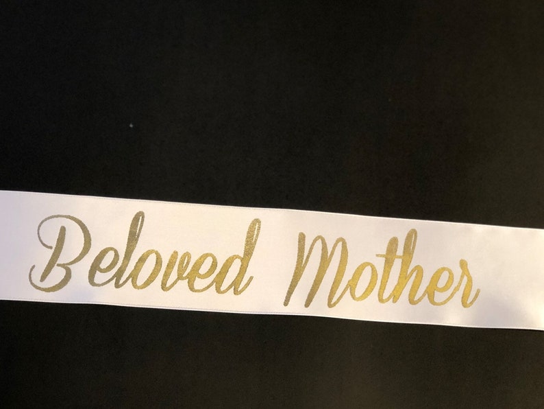 Puede incluir: Cinta de sat&eacute;n blanca con las palabras "Beloved Mother" escritas en letras doradas cursivas.