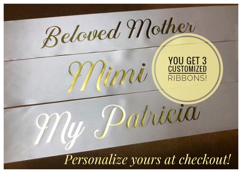 Puede incluir: Tres cintas de sat&eacute;n blanco con letras doradas. Las cintas dicen "Beloved Mother", "Mimi" y "My Patricia". El texto "YOU GET 3 CUSTOMIZED RIBBONS!" est&aacute; en un c&iacute;rculo en la imagen. &iexcl;Personaliza las tuyas en la caja!