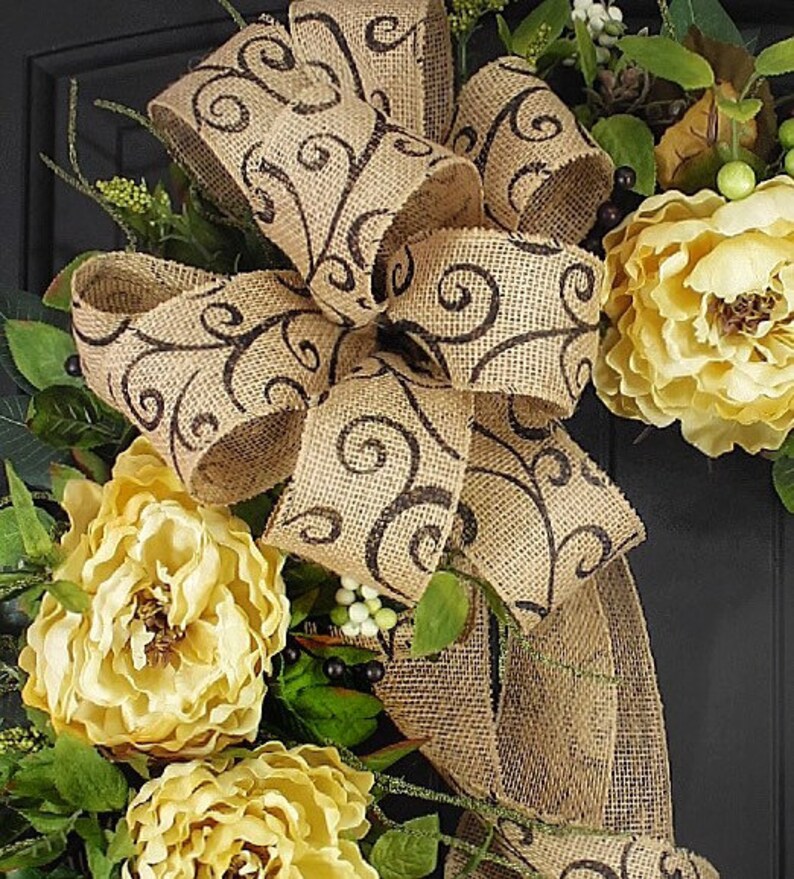 Pode incluir: Uma coroa de juta com um grande la&ccedil;o marrom com um padr&atilde;o de espiral. A coroa &eacute; decorada com flores de seda amarelas e folhas verdes.