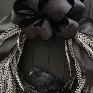 May include: A black wreath with a black satin bow and silver-grey sprigs. A black raven sits in the center of the wreath.