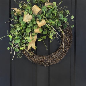May include: A green eucalyptus wreath with a burlap bow. The wreath is hanging on a black door.