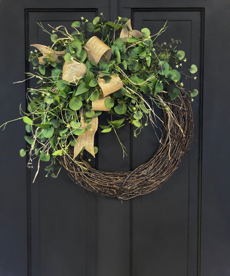 May include: A green eucalyptus wreath with a burlap bow. The wreath is hanging on a black door.