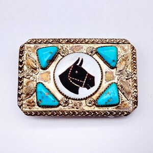 May include: Rectangular silver-toned belt buckle with a horse head design. The buckle features a black horse head on a white background, surrounded by turquoise stones and decorative metalwork. The buckle has a detailed, vintage appearance.