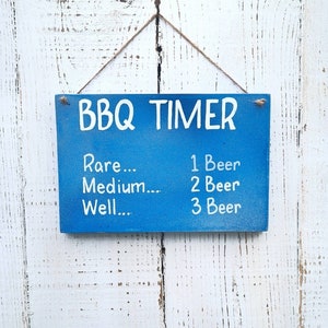 May include: Blue wooden sign with white text that reads "BBQ TIMER". The sign lists different levels of doneness for meat, with corresponding numbers of beers to drink while waiting.