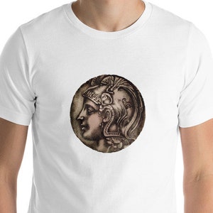 May include: White t-shirt featuring a circular graphic of a classical profile in shades of brown and gray. The graphic is centered on the chest. The t-shirt is short-sleeved and has a crew neck.