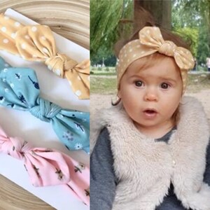 May include: Three fabric headbands with different patterns. The first headband is yellow with white polka dots, the second is blue with white flowers, and the third is pink with white flowers. The headbands are tied in a bow at the top.