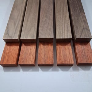 May include: A collection of rectangular wooden blocks in varying shades of brown and reddish-brown. The blocks are arranged in a row, showcasing the natural wood grain and color variations. The image highlights the texture and tones of the wood.