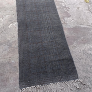 May include: A rectangular, dark gray rug with a woven texture and a subtle grid pattern. The rug has a fringe detail on the shorter ends. The rug is approximately 60 inches long and 24 inches wide. The rug is suitable for a hallway or entryway.