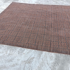 May include: A large, rectangular rug with a repeating floral pattern in dark brown on a lighter brown background. The rug has a border with a similar design. The rug is placed on a concrete surface.