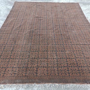 May include: A large, rectangular rug with a repeating floral pattern in dark brown and black. The rug has a fringe along the bottom edge and is made of a woven material. The rug's color palette is primarily brown and black.