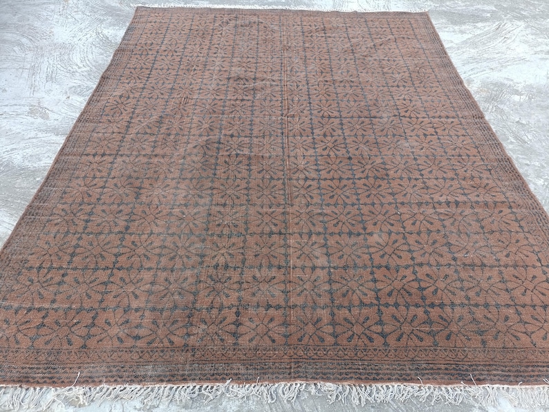 May include: A large, rectangular rug with a repeating floral pattern in dark brown and black. The rug has a fringe along the bottom edge and is made of a woven material. The rug's color palette is primarily brown and black.