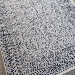 May include: A white rug with a blue floral pattern. The rug has a border with a repeating geometric design.