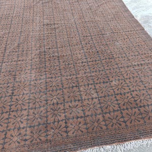 May include: A rectangular brown rug with a repeating floral pattern in dark brown. The rug has a fringe along the bottom edge and a decorative border. The rug is likely made of wool and is suitable for a living room or bedroom.