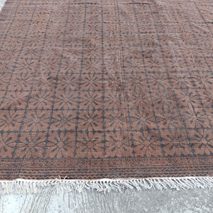 May include: Brown and black patterned rug with a floral design. The rug has a rectangular shape and a fringe along the bottom edge. The pattern is repeated across the surface.