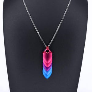 May include: A silver chain necklace with a pendant featuring a series of heart-shaped scales in pink, magenta, purple, and blue. The pendant is suspended from a delicate silver chain, creating a striking and colorful accessory.