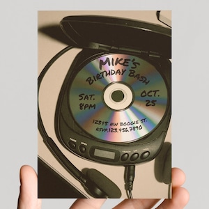 Könnte beinhalten: Ein schwarzer tragbarer CD-Player mit einer silbernen Disc im Inneren. Auf der Disc steht "Mike's Birthday Bash" mit Datum und Uhrzeit. Ein Paar schwarze Kopfhörer ist angeschlossen. Die RSVP-Telefonnummer ist ebenfalls sichtbar.