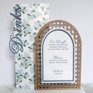 May include: A decorative drinks menu with a floral patterned background and a wooden frame. The menu lists "On Draft", "Wines", and "Seltzer" options. The word "Drinks" is displayed in a cursive font.