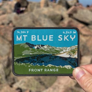 May include: A rectangular patch with a blue sky background and the words "MT BLUE SKY" in white. The patch also features a mountain landscape illustration and the text "FRONT RANGE". The patch measures 14,264 F and 4,347 M.