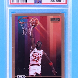 May include: A 1990 Skybox Michael Jordan basketball card graded PSA 9. The card features a photo of Michael Jordan in a red and white Chicago Bulls uniform, dunking a basketball. The card has a gold background with a red and white striped pattern.